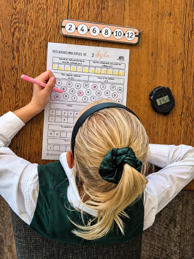 Learner working through a multilingual multiples worksheet at a desk with learning tools