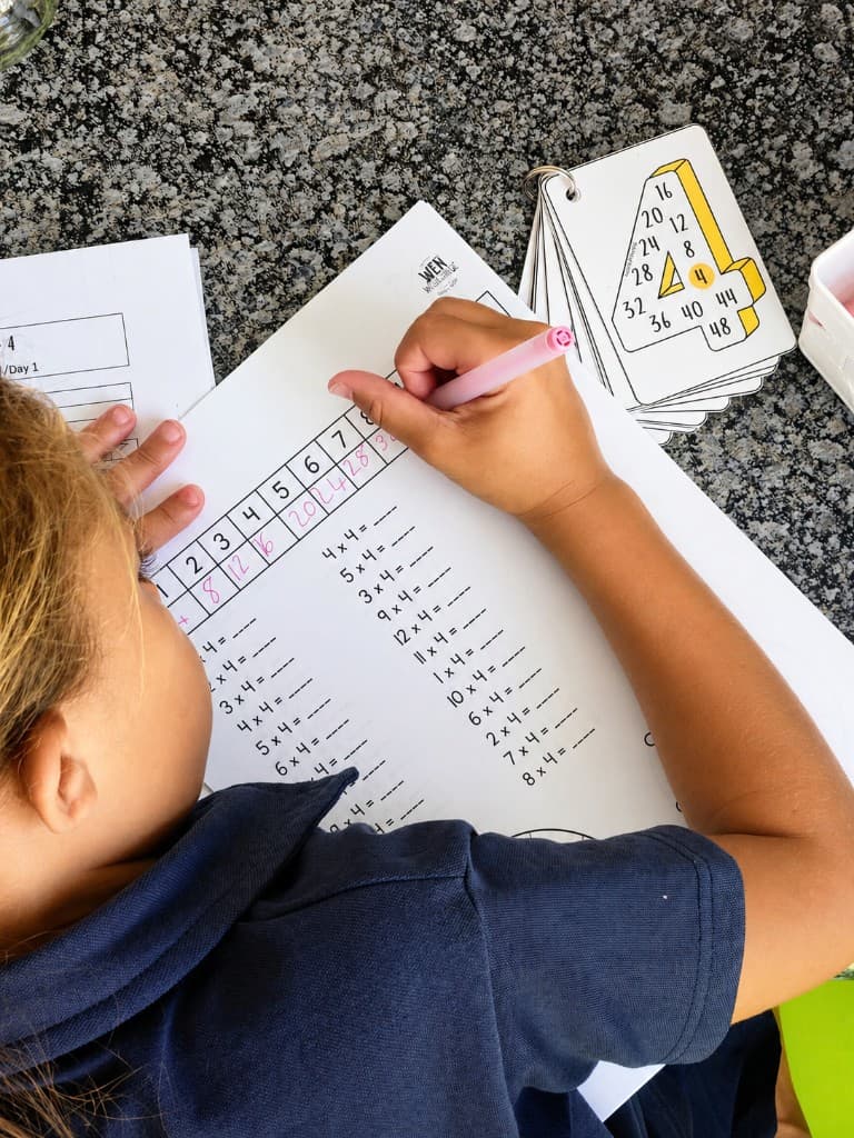 Learner working on multiples with ring flashcards stacked beside the page